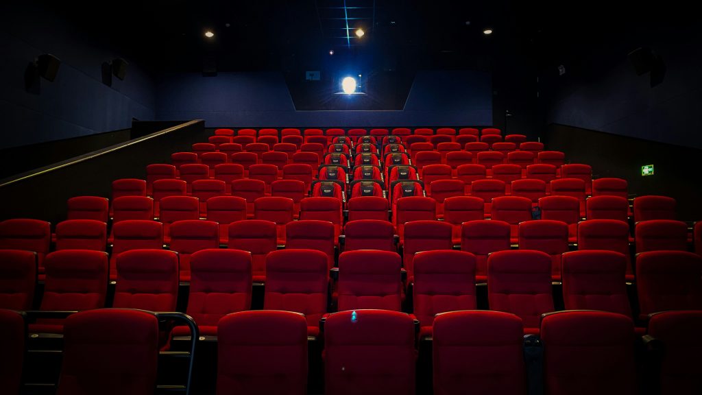 An empty cinema with rows of red seats facing the screen