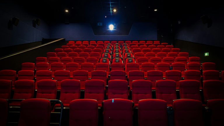 An empty cinema with rows of red seats facing the screen