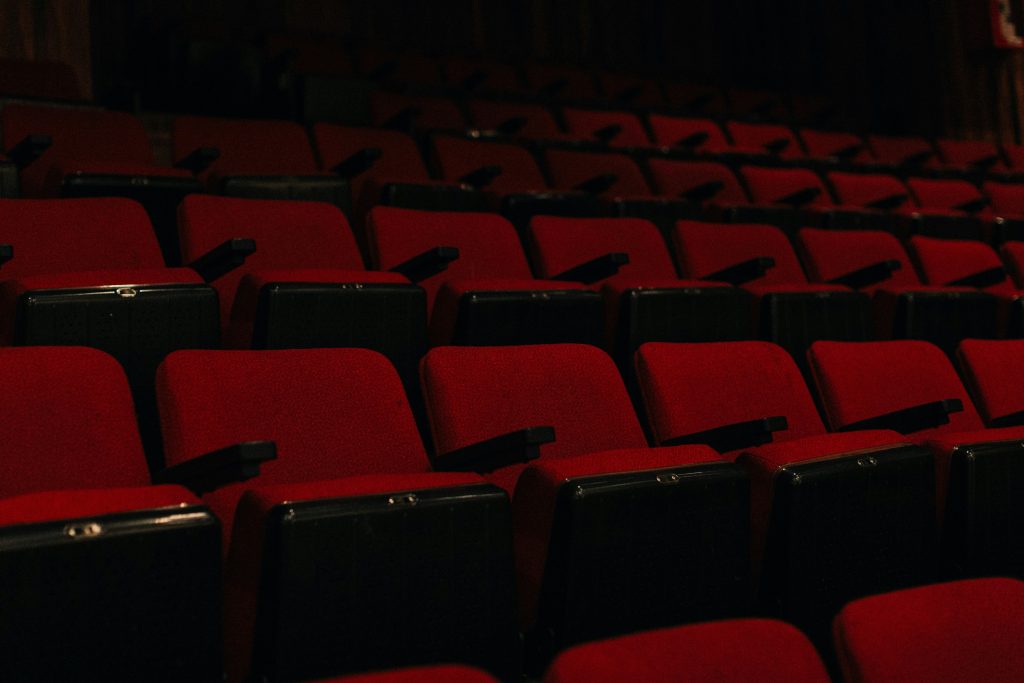 A large empty auditorium with rows of red seats in low light
