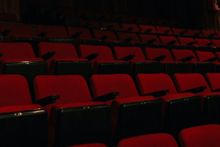 A large empty auditorium with rows of red seats in low light